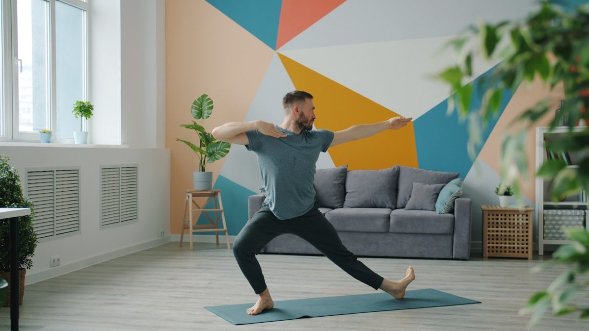 Professional yoga instructor in sports clothing is exercising at home doing complex of asanas alone standing on mat. Activity and apartment concept.